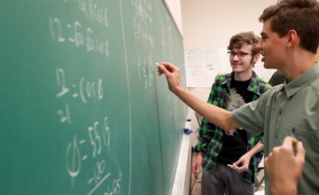 People solving problems on a blackboard in a classroom