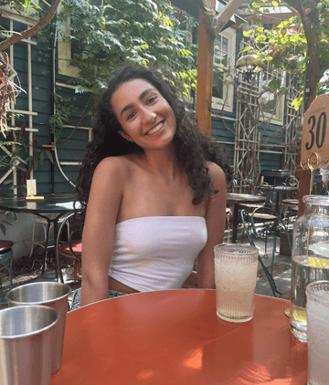 A woman sitting at a table with a drink smiling at the camera
