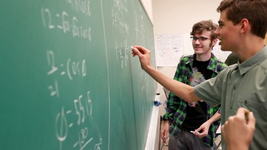 People solving problems on a blackboard in a classroom