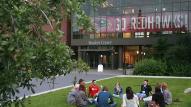 Students gathered and seated on the grass in conversation in front of Lemieux Library.