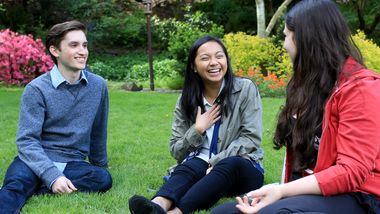 Three students sit on the lawn