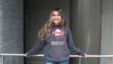 A student leaning against a railing, wearing an SU hoodie