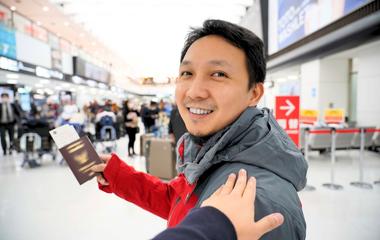 An Asian student holding a passport in an airport