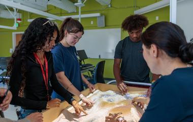Students move around sand in a table with topographic projections