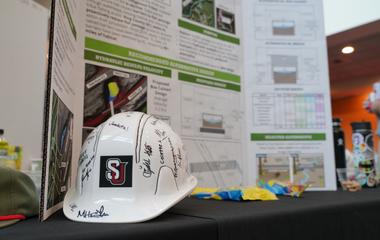 White hard hat with SU letters on front and a research poster as background