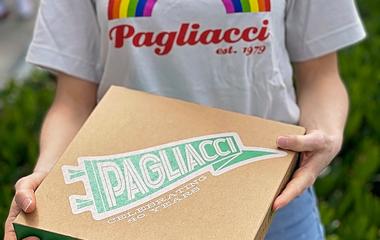 A person wearing a Pagliacci t-shirt with a rainbow holding a box that says Pagliacci 1979