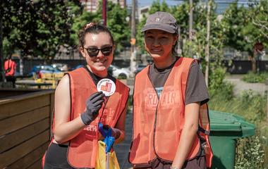 Two people posing in safety vests with one holding up an SU Day of Service sticker.