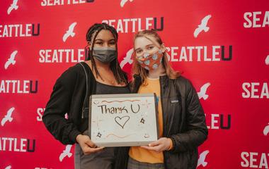 Two people standing in front of a seattle-themed backdrop holding a sign with 