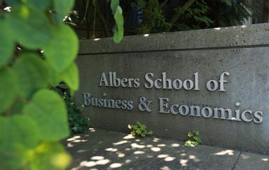 Sign for albers school of business & economics partially shaded by foliage.