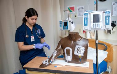 A healthcare professional prepares medical equipment beside a patient simulator in a clinical training environment.