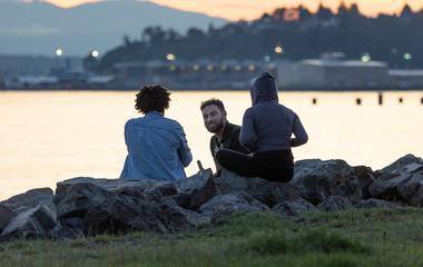 Three people sitting on rocks by a body of water at dusk.