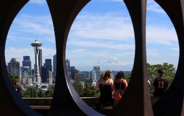 View of the seattle skyline with the space needle framed by circular openings, as people observe from a distance.