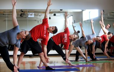 Group of individuals participating in a yoga class, performing a side stretch pose.