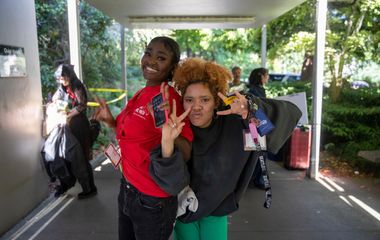 Two people posing for a photo with a peace sign gesture at a bus stop.