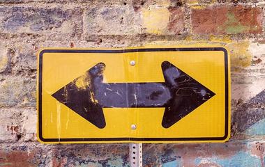 Photo of a two-way arrow street sign against a brick wall