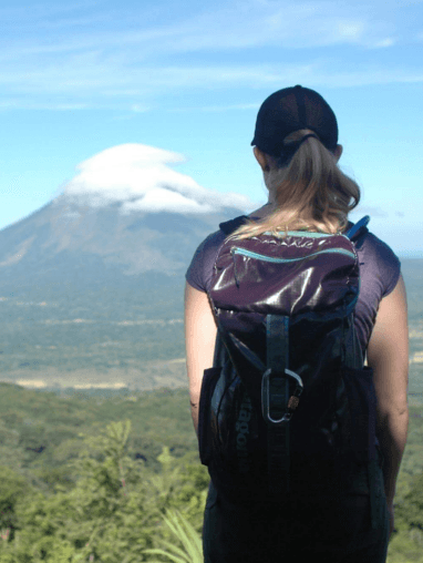 he back of a woman with a backpack viewing the large mountain in the background