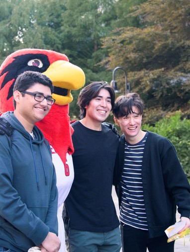three students standing with mascot Rudy the Redhawk