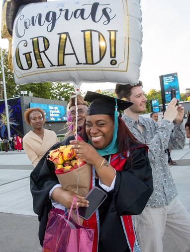 Female student in cap and gown holding a bouquet of flowers and balloon
