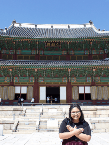 Student with Redhawk sign in front of Korean Temple