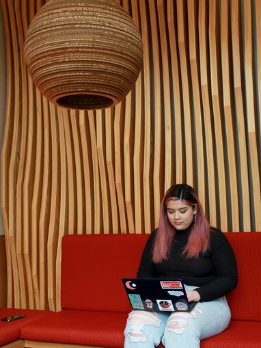A woman sitting on a red couch with a laptop.