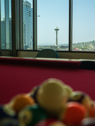 The Space Needle in the distance through a high window at the Cornish Commons, with a pool table and balls obscured in the foreground.