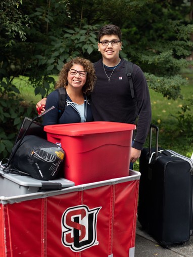 Students moving into the dorm with a large bin of stuff