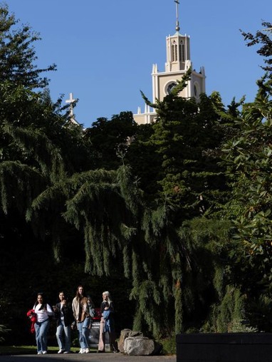 A group of people walking through a park with a clock tower in the background.
