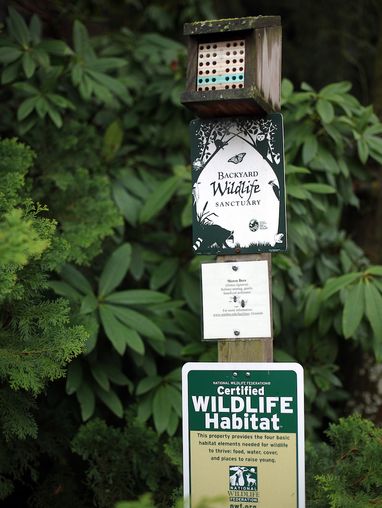 a post with a mason bee house and several wildlife sanctuary and habitat signs