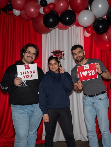 three students in the SU Gives photo booth holding I heart SU signs