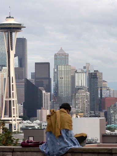 A woman sits on a ledge overlooking the seattle skyline.