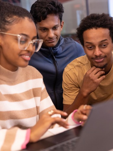 a group of 3 students looking at the same laptop screen smiling