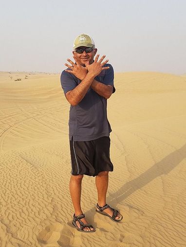Madhu Rao doing the Red Hawk sign while standing on a dune in Dubai