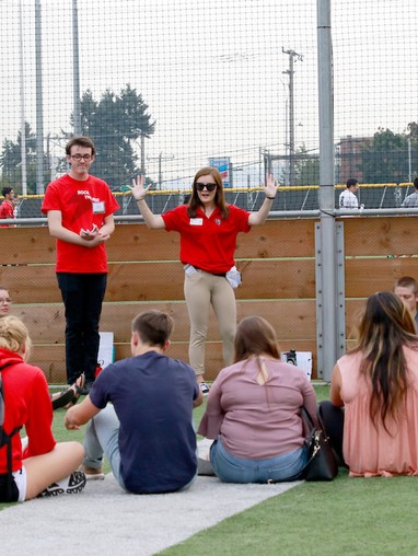 2 orientation leaders in red polos leading an activity with new students sitting in a circle