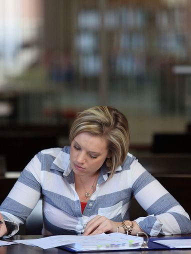 Woman studying at a library table with books and papers.