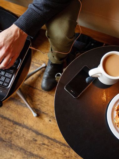 Person working on a laptop at a coffee table with a cup of coffee and a pastry.