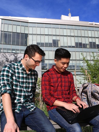 Two students sitting on a bench in front of a building.