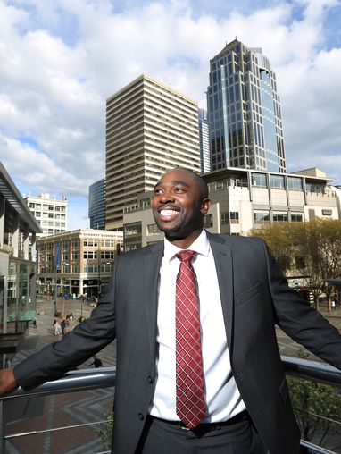 MBA grad Terren Drake smiling and standing on a balcony amidst the buildings of downtown Seattle