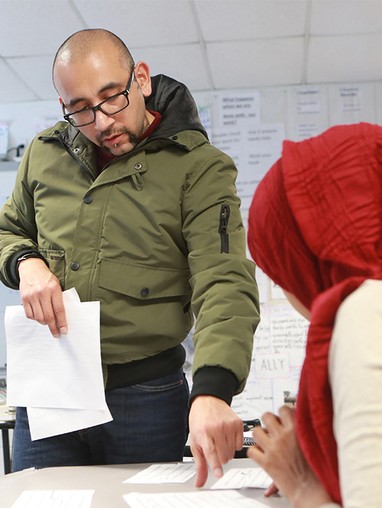 Standing teacher points to paper to help student sitting at their desk.