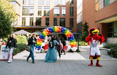 Mascot and students in front of colorful baloon arch