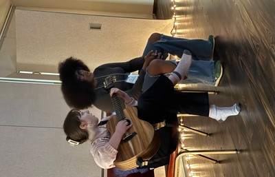 Two students seated, one playing the guitar the other singing