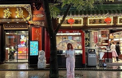 Woman holding an umbrella standing on the curb side in front of a store