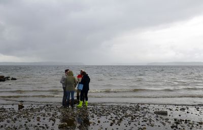 People standing in a huddle on the shore of the ocean