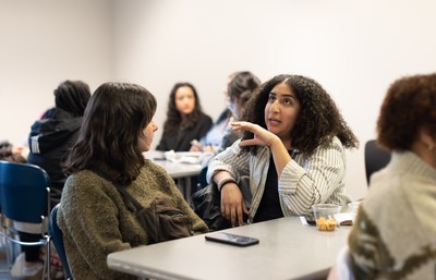 Two people sitting at a classroom table engaged in discussion.