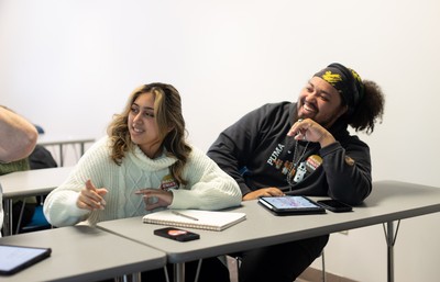 Two people sitting at a classroom table and smiling.