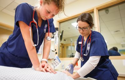 Two students in scrubs practicing in a clinical lab