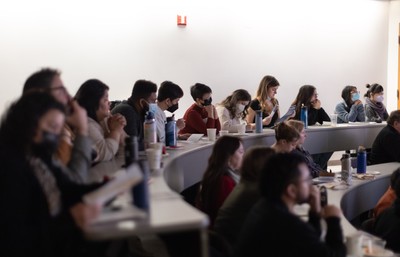 A classroom full of students, faculty and staff, watching looking at the screen at the front of the room.