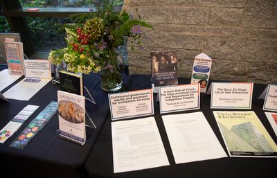 Photo of a table with black tablecloth. On the table there is a flowers bouquet, a few books and papers of academic articles.