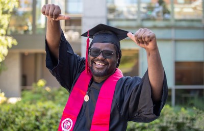 Graduating student in full grad regalia fists in air and smiling