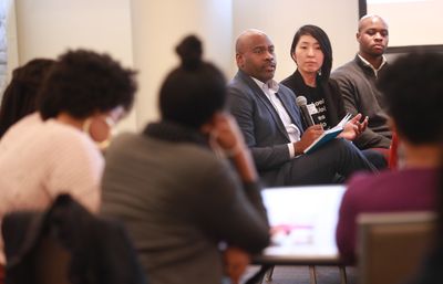 Alvin Sturdivant sitting in a chair, holding a microphone, and speaking to a group of people sitting next to him.