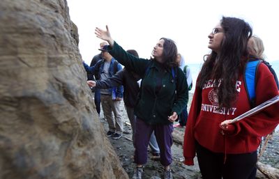 A professor points at a rock formation as a student looks up at it